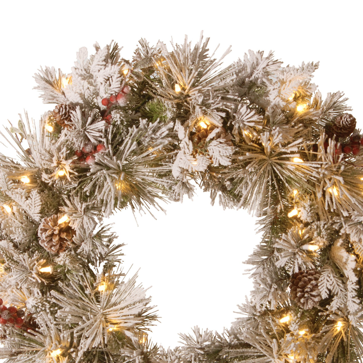 Close-up snowy wreath foliage with warm LED lights, pine cones and red berry accents.
