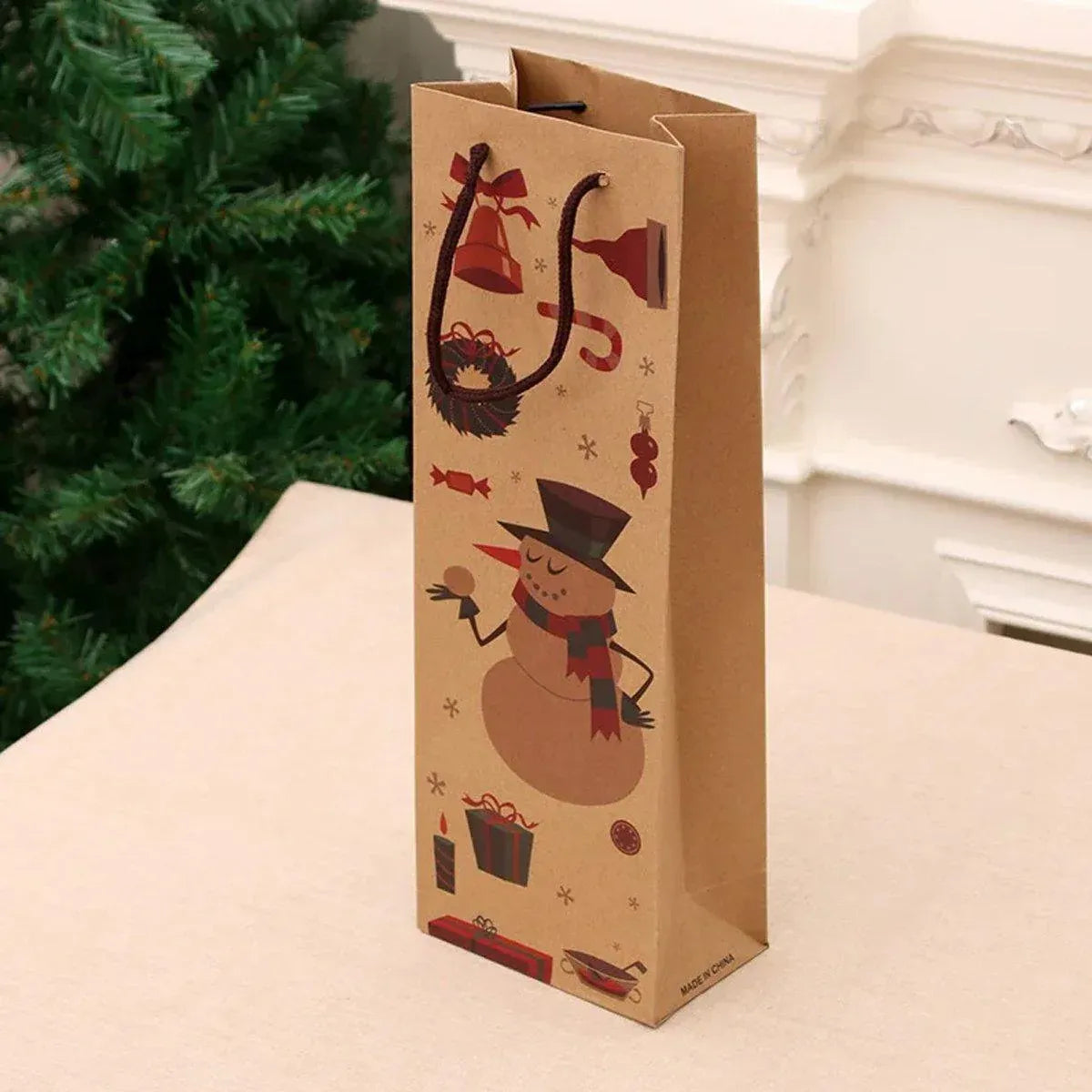 Kraft wine bottle gift bag with snowman illustration placed beside a Christmas tree