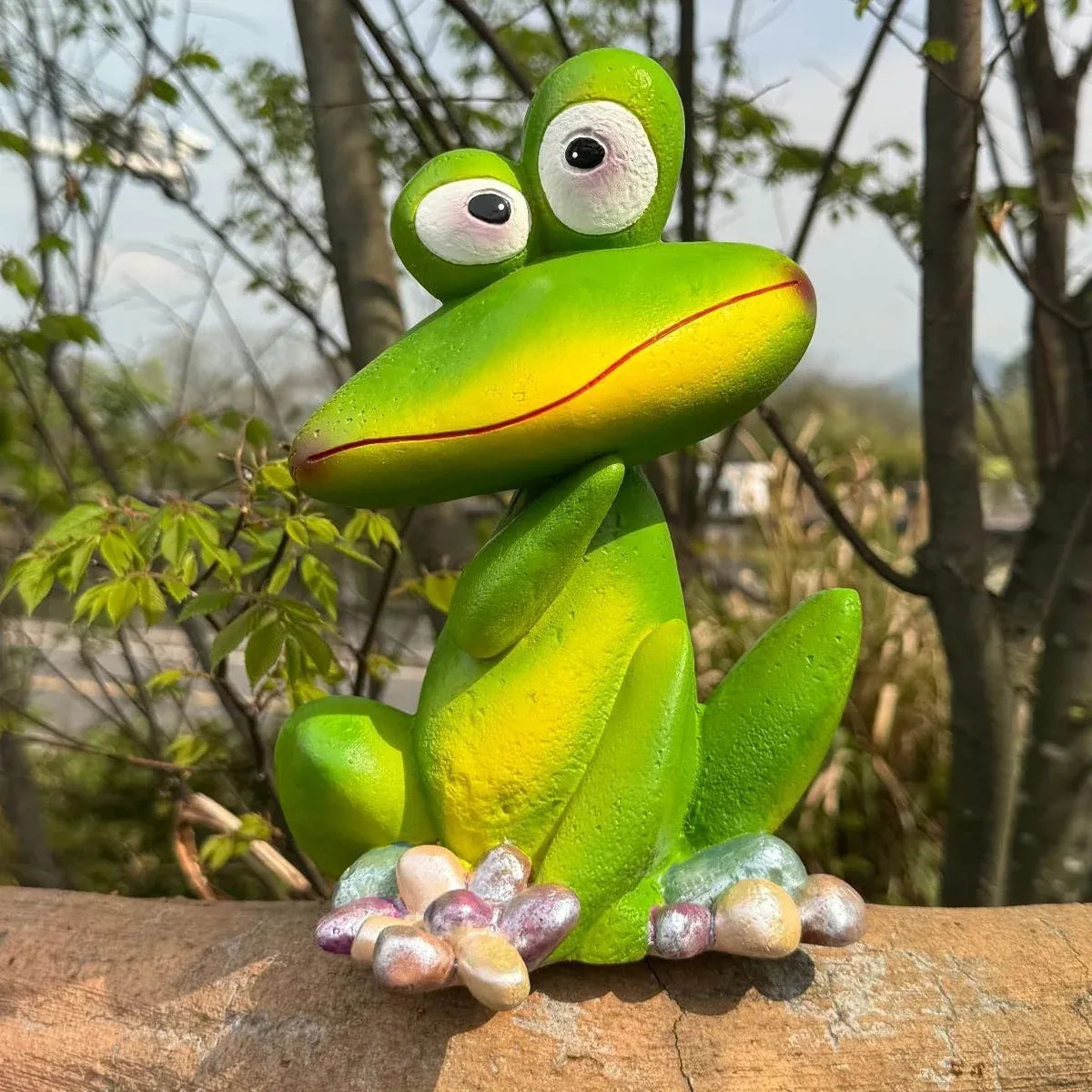 Green frog garden ornament statue on wooden surface, glossy eyes and pebble-flower base