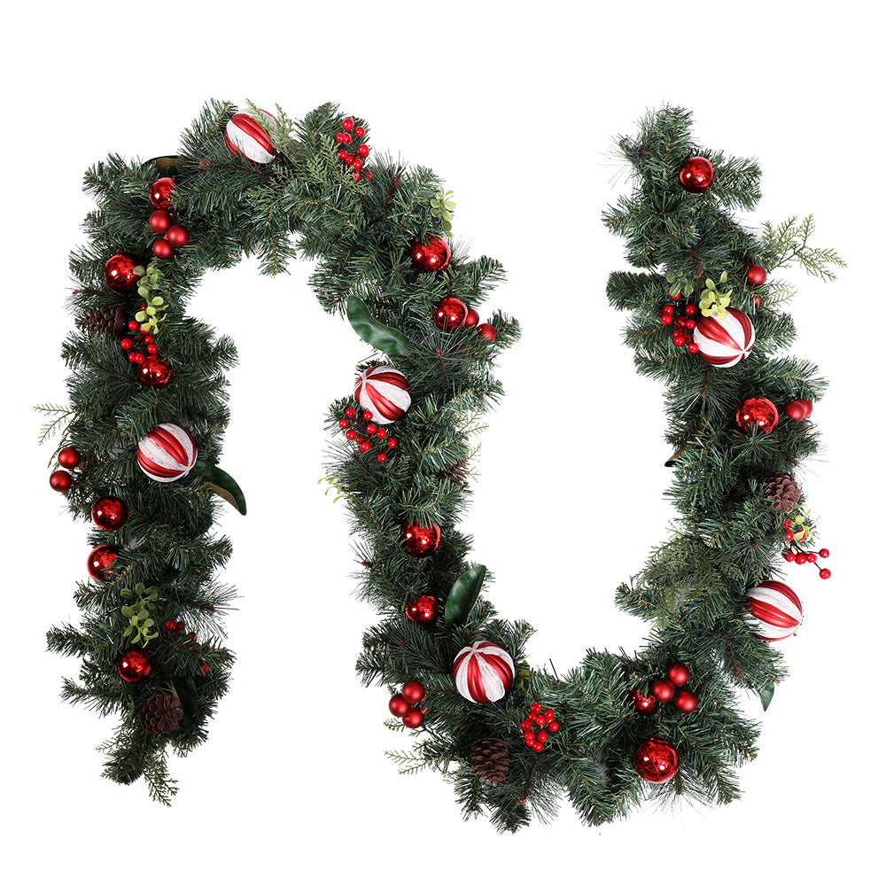 Artificial Christmas garland with dark green pine and red baubles, bows, and ribbon