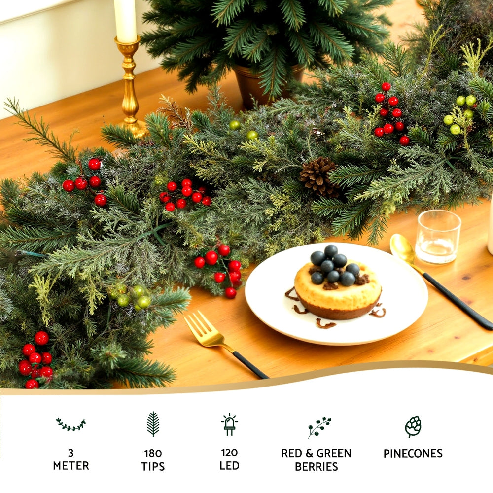 Lit Christmas garland with pine cones and red berries draped over tabletop setting