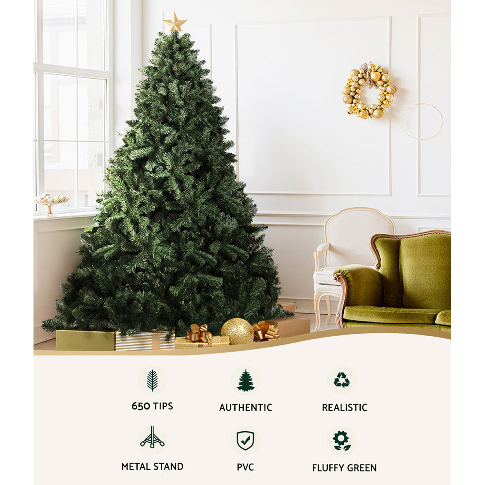 Decorative Christmas tree in a living room with a green sofa and wreath on a white wall.