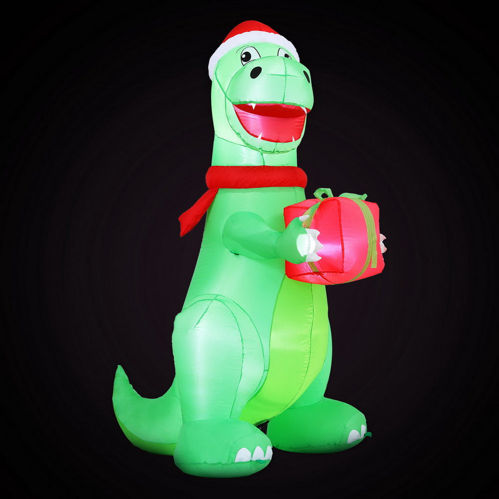 Inflatable green dinosaur with Santa hat and red scarf, holding a pink gift