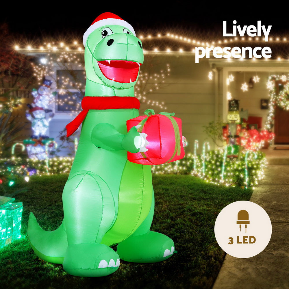Inflatable green dinosaur with Santa hat and red scarf, holding pink gift with LED lights