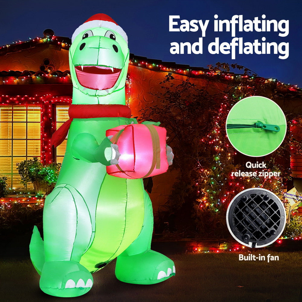 Inflatable green dinosaur with Santa hat holding a pink gift, glossy body, LED lights
