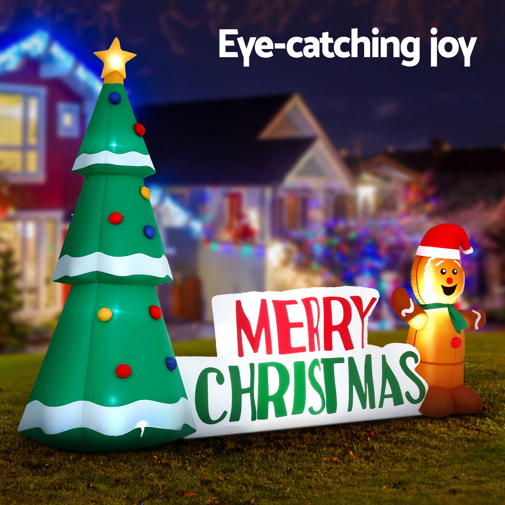 Inflatable green Christmas tree with LED lights and Merry Christmas sign next to gingerbread figure