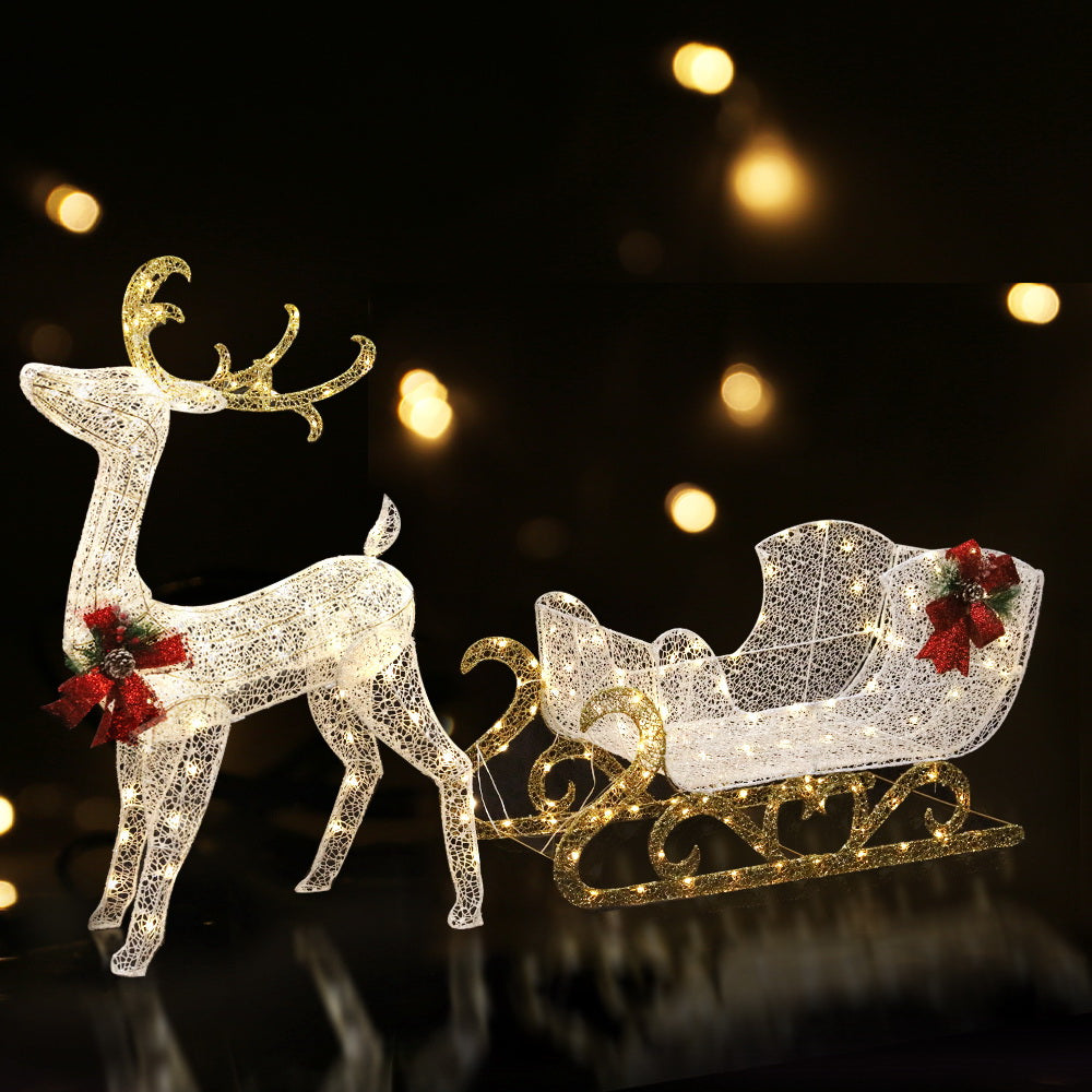 Warm LED-lit white reindeer pulling gold sleigh with red bow accents